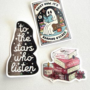 May include: Three stickers with a literary theme. One sticker features a ghost reading a book with the text "QUIET NOW, IT'S READING O'CLOCK". Another sticker says "to the stars who listen". The third sticker shows a stack of books and a candle.