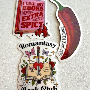 May include: Three stickers: a pink book with text "I LIKE MY BOOKS EXTRA SPICY" and flames, a red chili pepper with "HIGH SPICE TOLERANCE", and a book with a sword through a heart, butterflies, and text "Romantasy Book Club".