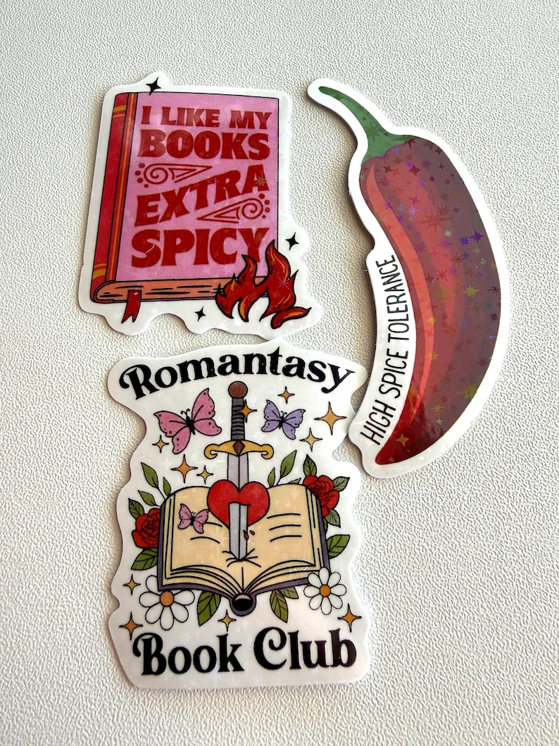 May include: Three stickers: a pink book with text "I LIKE MY BOOKS EXTRA SPICY" and flames, a red chili pepper with "HIGH SPICE TOLERANCE", and a book with a sword through a heart, butterflies, and text "Romantasy Book Club".