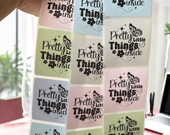 May include: A roll of stickers with a repeating pattern of square stickers. Each sticker has a light blue, light green, or pink background with a black butterfly and the text "Pretty Little Things #inside".