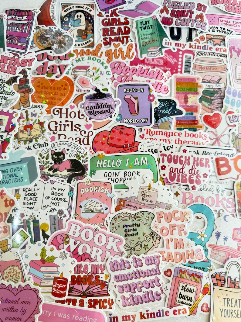 May include: A collection of colorful stickers with various book-related themes. The stickers feature phrases like "Bookish," "Hot Girls Read," and "Fueled by Smut and Coffee." Designs include stacks of books, cats, and hearts, with a mix of fonts and styles.