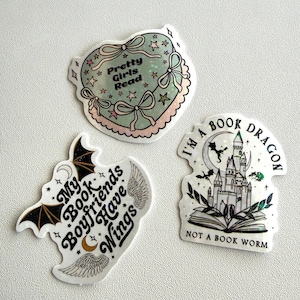 May include: Three stickers with book-themed designs. One is heart-shaped with the text "Pretty Girls Read". Another features a bat and the text "My Book Boyfriends Have Wings". The third shows a castle and the text "I'm a Book Dragon, Not a Book Worm".