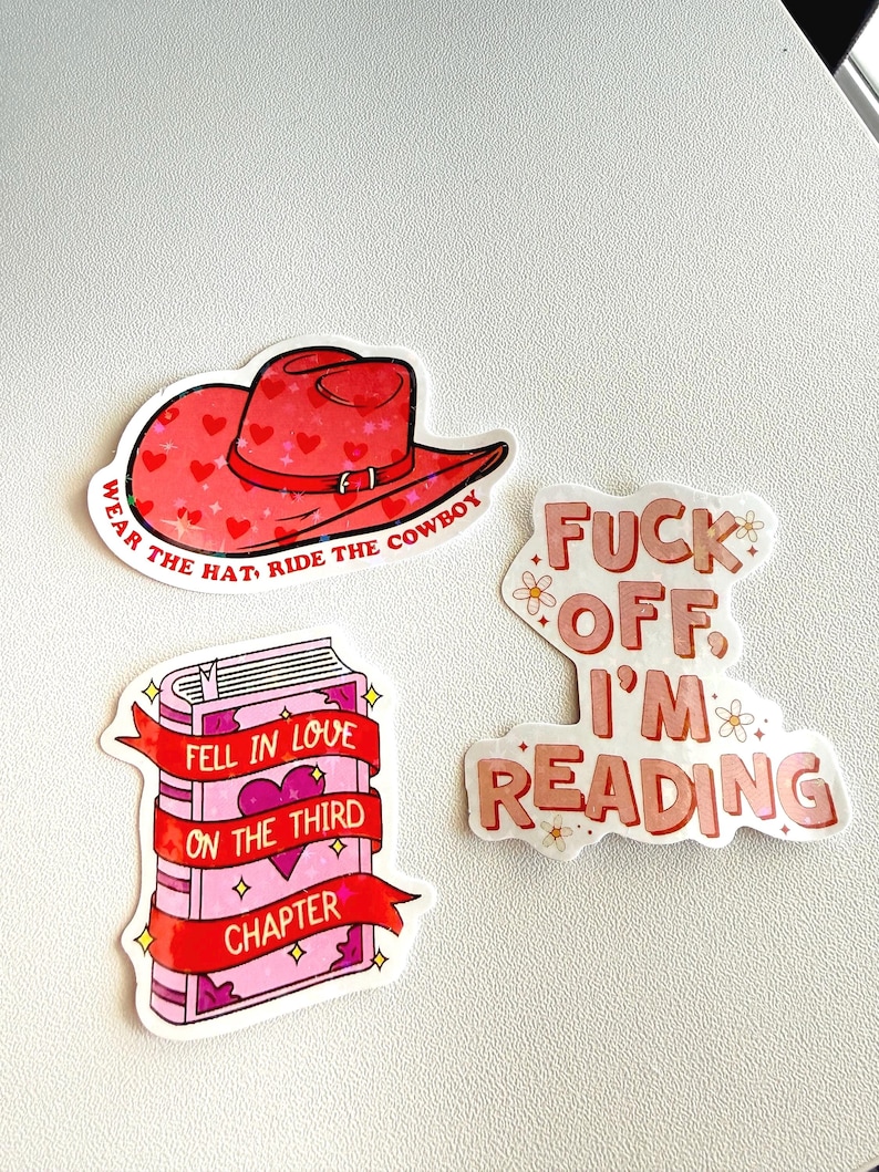 May include: A collection of stickers with a reading theme. One sticker features a red cowboy hat with heart accents and the text "WEAR THE HAT, RIDE THE COWBOY." Another shows a pink book with the text "FELL IN LOVE ON THE THIRD CHAPTER."