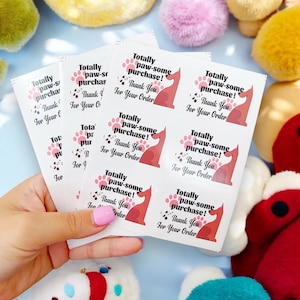 May include: A sheet of stickers with a pink and black paw print design. The stickers say "Totally paw-some purchase! Thank you for your order."