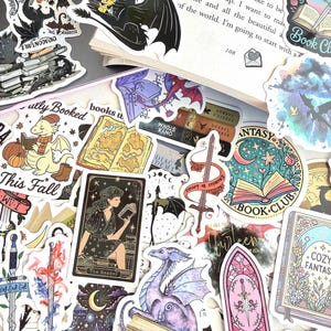 May include: A collection of fantasy-themed stickers featuring dragons, books, swords, and celestial elements. The stickers showcase various designs, including a dragon reading a book, a tarot card with a woman reading, and the text "Book Club."