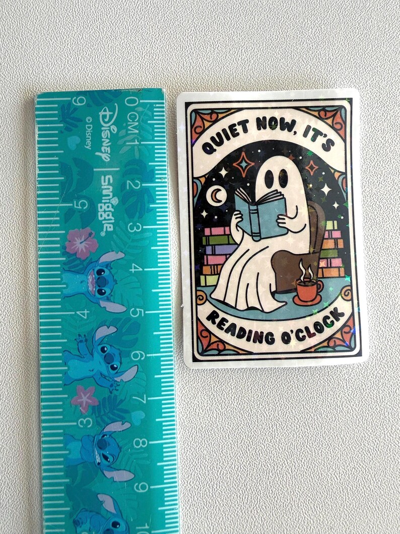 May include: A rectangular sticker featuring a cartoon ghost reading a book in a chair, with the text "QUIET NOW, IT'S READING O'CLOCK". The sticker is approximately 3 inches tall and 2 inches wide.