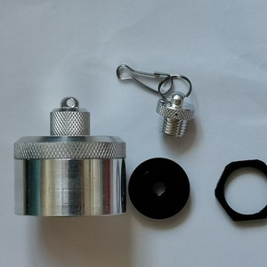 Könnte beinhalten: Ein silberner Flaschenverschluss aus Metall mit einer kleinen Schlaufe oben, ein silberner Verschluss aus Metall mit einem Gewindeende, ein schwarzer Plastikverschluss mit einem Loch in der Mitte und ein schwarzer sechseckiger Ring aus Plastik.