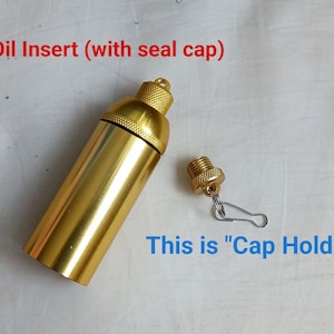 May include: Gold metal oil insert with a cap holder. The oil insert is a small, cylindrical container with a screw-on cap. The cap holder is a small, metal loop attached to the cap.