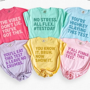 May include: A collection of six colorful t-shirts in shades of pink, blue, green, yellow, and purple. Each shirt features a unique, bold text design with phrases like "The Vibes Don't Lie" and "You Know It. Bruh."