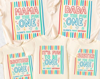 May include: Cream-colored t-shirts with colorful text and graphics. The shirts read "MAMA," "DADA," "BROTHER," "IT'S FUN TO BE," and "SISTER" with "ONE" and "Oliver's First Birthday." The shirts have vertical stripes.