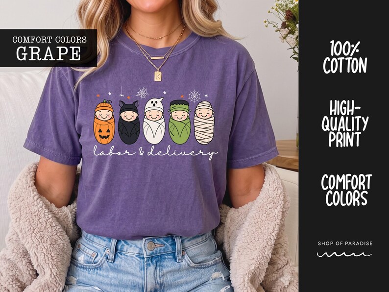 K&ouml;nnte beinhalten: Ein traubenfarbenes Kurzarm-T-Shirt mit einer Grafik von f&uuml;nf in Windeln gewickelten Babys, die als K&uuml;rbis, Fledermaus, Geist, Frankensteins Monster und Mumie verkleidet sind. Der Text "labor & delivery" steht in wei&szlig;er Schreibschrift darunter.