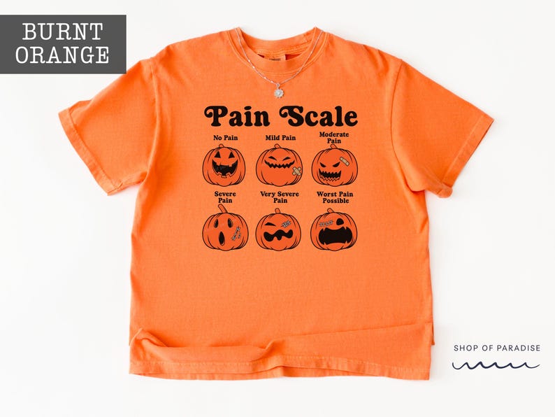 May include: A burnt orange short-sleeve t-shirt featuring a black graphic of six jack-o'-lanterns labeled as a Pain Scale. The text reads No Pain, Mild Pain, Moderate Pain, Severe Pain, Very Severe Pain, and Worst Pain Possible in black font.