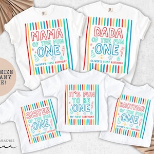 May include: White t-shirts with colorful text and graphics for a first birthday celebration. The shirts read "Mama," "Dada," "Sister," "It's Fun to be One," and "Brother" with the name "Oliver's First Birthday." The shirts have vertical stripes.