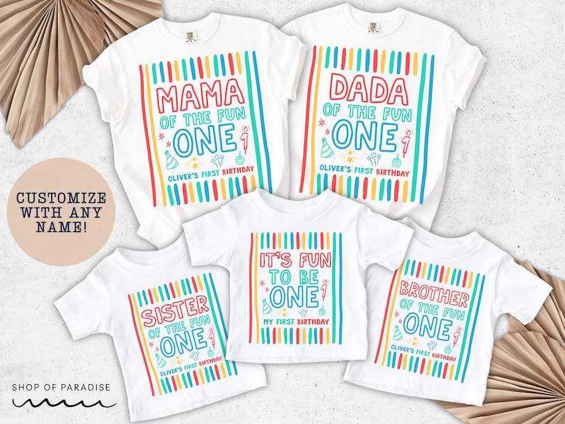 May include: White t-shirts with colorful text and graphics for a first birthday celebration. The shirts read "Mama," "Dada," "Sister," "It's Fun to be One," and "Brother" with the name "Oliver's First Birthday." The shirts have vertical stripes.