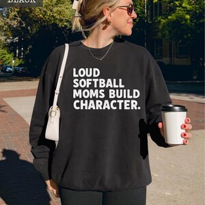 May include: Black sweatshirt with the text "LOUD SOFTBALL MOMS BUILD CHARACTER" in white. The sweatshirt is a Comfort Colors 1466 Lightweight Sweatshirt.