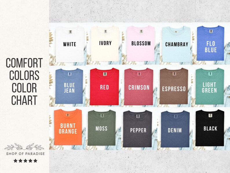 May include: A color chart displaying a variety of Comfort Colors t-shirts. The shirts are arranged in rows and columns, showcasing colors like white, ivory, blossom, chambray, and flo blue. The chart includes the text "Comfort Colors Color Chart" and the Shop of Paradise logo.