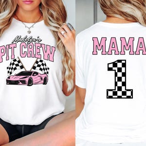 May include: Two white t-shirts with a racing theme. The front shirt says "Madelyn's Pit Crew" with a pink race car and checkered flags. The back shirt says "MAMA" with a large pink number "1" with a checkered flag design.