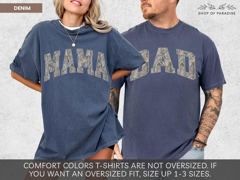 Puede incluir: Dos camisetas de color denim. Una dice "MAMA" y la otra "DAD" en una fuente de estilo camuflaje. Las camisetas forman parte de la colecci&oacute;n Comfort Colors. El logotipo de Shop of Paradise est&aacute; en la esquina superior derecha.