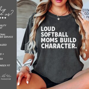 May include: Dark gray t-shirt with the text "LOUD SOFTBALL MOMS BUILD CHARACTER" in white. The shirt also features the text "COMFORT COLORS PEPPER". The shirt is part of the Shop of Paradise collection.