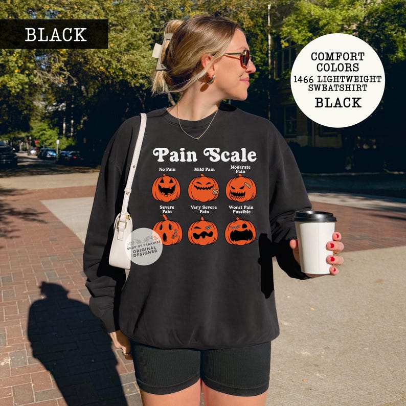 May include: A black long-sleeve sweatshirt featuring a graphic of six orange jack-o'-lanterns arranged in a grid. The text reads Pain Scale, with labels for No Pain, Mild Pain, Moderate Pain, Severe Pain, Very Severe Pain, and Worst Pain Possible.