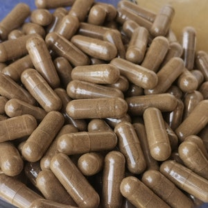 May include: A close-up view of a large quantity of brown capsules in a clear glass bowl. The capsules are translucent and filled with a brown powder.