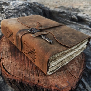 May include: A brown leather-bound journal with a keyhole design and a metal key attached. The journal is closed and has a rustic, vintage look.