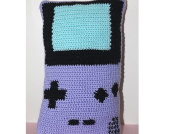 May include: A purple crocheted pillow shaped like a Game Boy with a teal screen and black buttons.