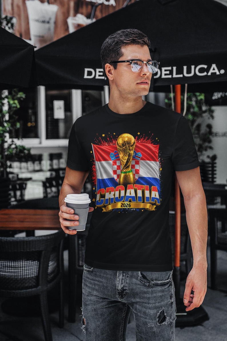 Black t-shirt worn by a male model featuring a Croatia football-themed design with the FIFA World Cup trophy, Croatian flag, and bold “CROATIA 2026” text on the front.