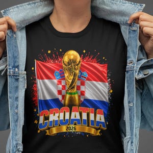Black t-shirt worn by a male model featuring a Croatia football-themed design with the FIFA World Cup trophy, Croatian flag, and bold “CROATIA 2026” text on the front.