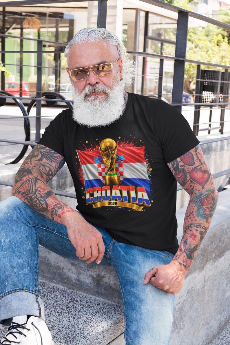 Black t-shirt worn by a male model featuring a Croatia football-themed design with the FIFA World Cup trophy, Croatian flag, and bold “CROATIA 2026” text on the front.