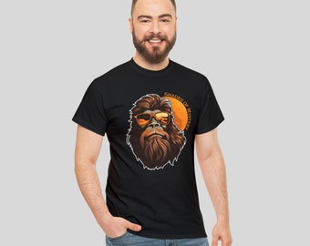 May include: A black t-shirt with a graphic of a cartoon Bigfoot wearing sunglasses and a sunset behind him. The text "Shades of Mystery" is written in a circle around the Bigfoot.
