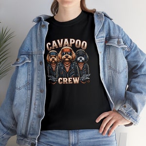 Puede incluir: Camiseta negra con un gráfico de tres perros Cavalier King Charles Spaniel con chaquetas de cuero y bandanas. El texto "Cavapoo Crew" está impreso debajo de los perros.