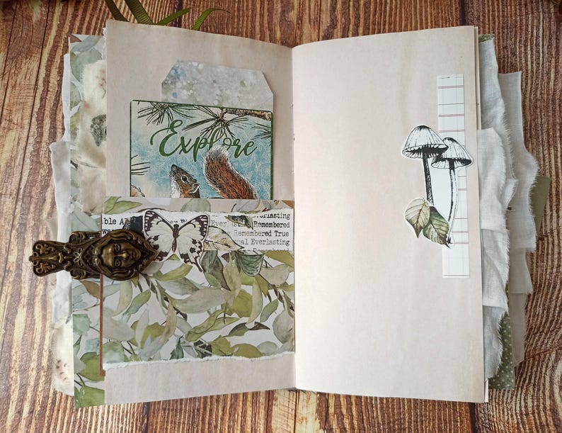 May include: Open journal with decorative elements. Features include a card with the word "Explore" and a squirrel illustration, a butterfly, and mushroom stickers. The journal is secured with a decorative clasp.