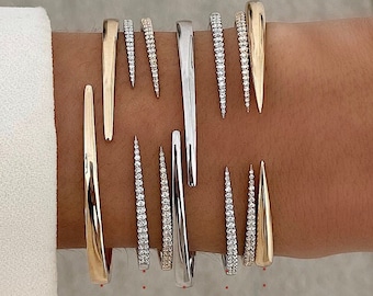 May include: A set of six gold and silver bracelets with pointed ends. Each bracelet is adorned with a row of small diamonds.