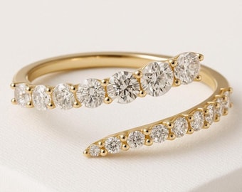 May include: A gold-colored ring with a spiral design. The ring is adorned with multiple clear, round-cut gemstones. The gemstones are set in a row along the ring's band, creating a sparkling effect. The ring is displayed on a white surface.