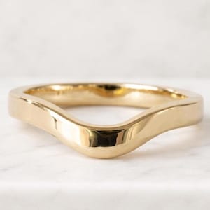 May include: A polished gold ring featuring a smooth, continuous band with a distinct V-shaped contour or wave design. The metal surface is highly reflective, showcasing a warm yellow tone and a seamless, solid construction throughout the band.