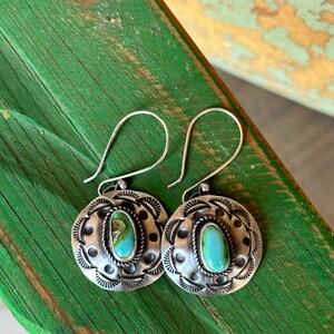 May include: A pair of silver earrings with turquoise stones set in a circular design. The earrings have a simple hook closure.