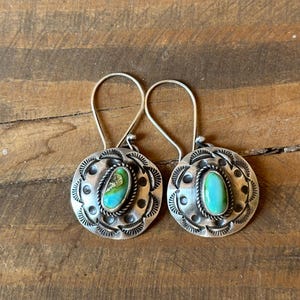 May include: A pair of silver earrings with turquoise stones set in a circular design. The earrings have a simple, elegant style.