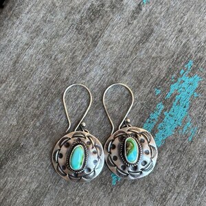 May include: A pair of silver earrings with turquoise stones set in a circular design. The earrings have a simple, elegant style.