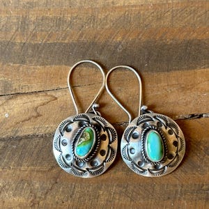 May include: A pair of silver earrings with turquoise stones set in a circular design. The earrings have a simple, elegant style.