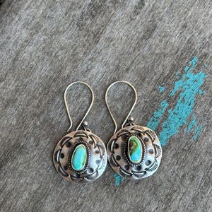 May include: A pair of silver earrings with turquoise stones set in a circular design. The earrings have a simple, elegant style.