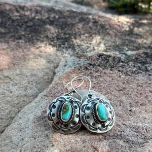 May include: A pair of silver earrings with turquoise stones set in a circular design. The earrings have a delicate, intricate pattern and are perfect for adding a touch of southwestern style to any outfit.