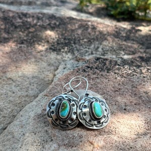 May include: A pair of silver earrings with turquoise stones set in a circular design. The earrings have a simple, elegant style.