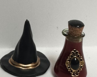 May include: A black witch's hat with a gold trim and a small red glass bottle with a black gemstone and gold accents.