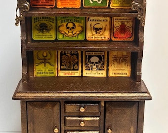 May include: A miniature wooden hutch with a glass-front top shelf and a lower cabinet with four drawers. The hutch is decorated with brass accents and features a collection of vintage-style apothecary labels with skull and insect imagery. The labels include text such as "Steedvioris", "Harannained", "Dransigium", and "Thedmelina".