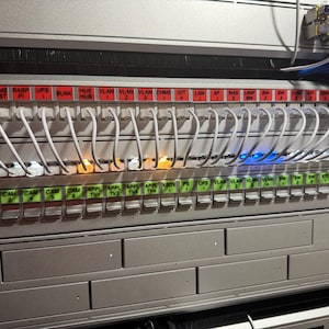 May include: A close-up of a network rack with multiple white ethernet cables plugged into ports labeled with various names, including "CAM", "WAVE", "RASP", "UPS", "BLNK", "HUE", "VLAN", "CHME", "IOT", "LAN", "NAS", "WMP", "SW", "CCTV", "INR", "INR", "MAC".