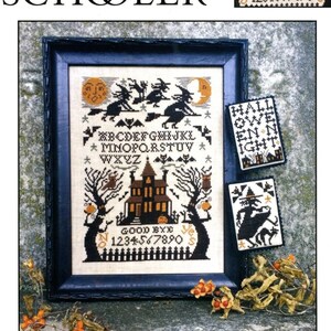 Op de afbeelding: Een ingelijste kruissteeksampler met een Halloween-thema. Het ontwerp toont heksen op bezems, een spookhuis, vleermuizen en de tekst "Witching Hour". Extra kleine kruissteekontwerpen zijn inbegrepen.