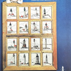 May include: A framed needlepoint chart titled "Lighthouses of the West Coast." The chart features a grid of small, detailed cross-stitch images of various lighthouses, each with unique designs and colors. A smaller, completed cross-stitch is in the upper left corner.