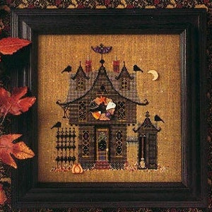 May include: A framed cross-stitch depicting a spooky house with three gables, ravens, and a crescent moon. The house is brown with orange and black accents, and a pumpkin sits at the base. The text "Three Gables" is at the bottom.