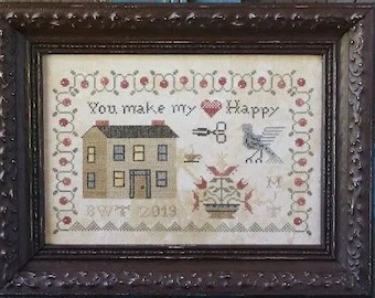 Op de afbeelding: Een ingelijst borduurwerk met een huis, bloemen, een vogel en de tekst "You make my heart happy".